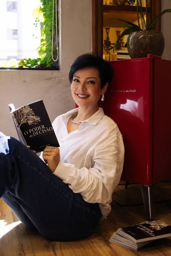 Lilian Vieira, fundadora da Escola de Protagonismo, sorridente, segurando o livro O Poder da Decisão